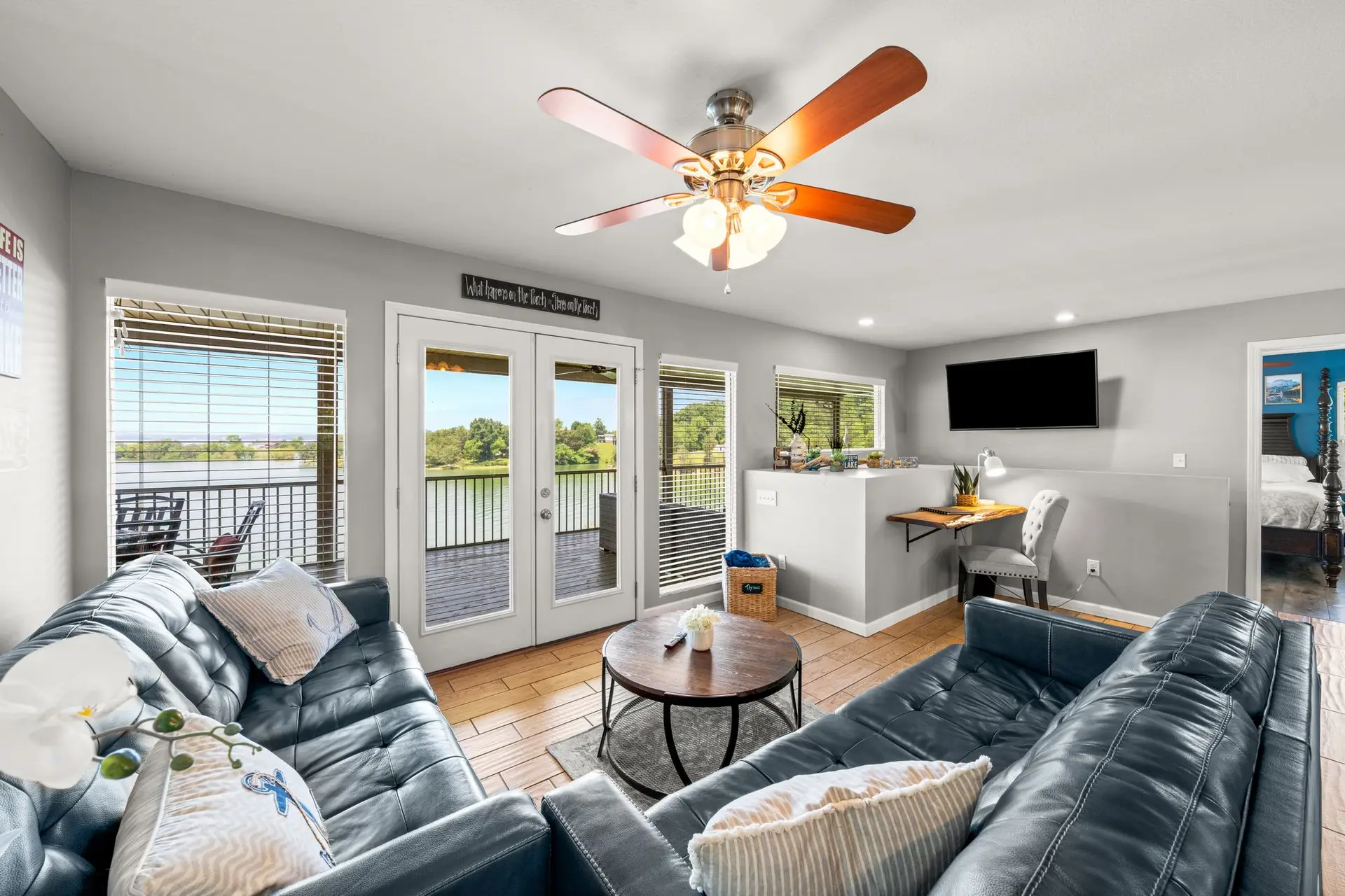 The living room sectional facing the mounted TV, with the screened porch and lake through the french doors