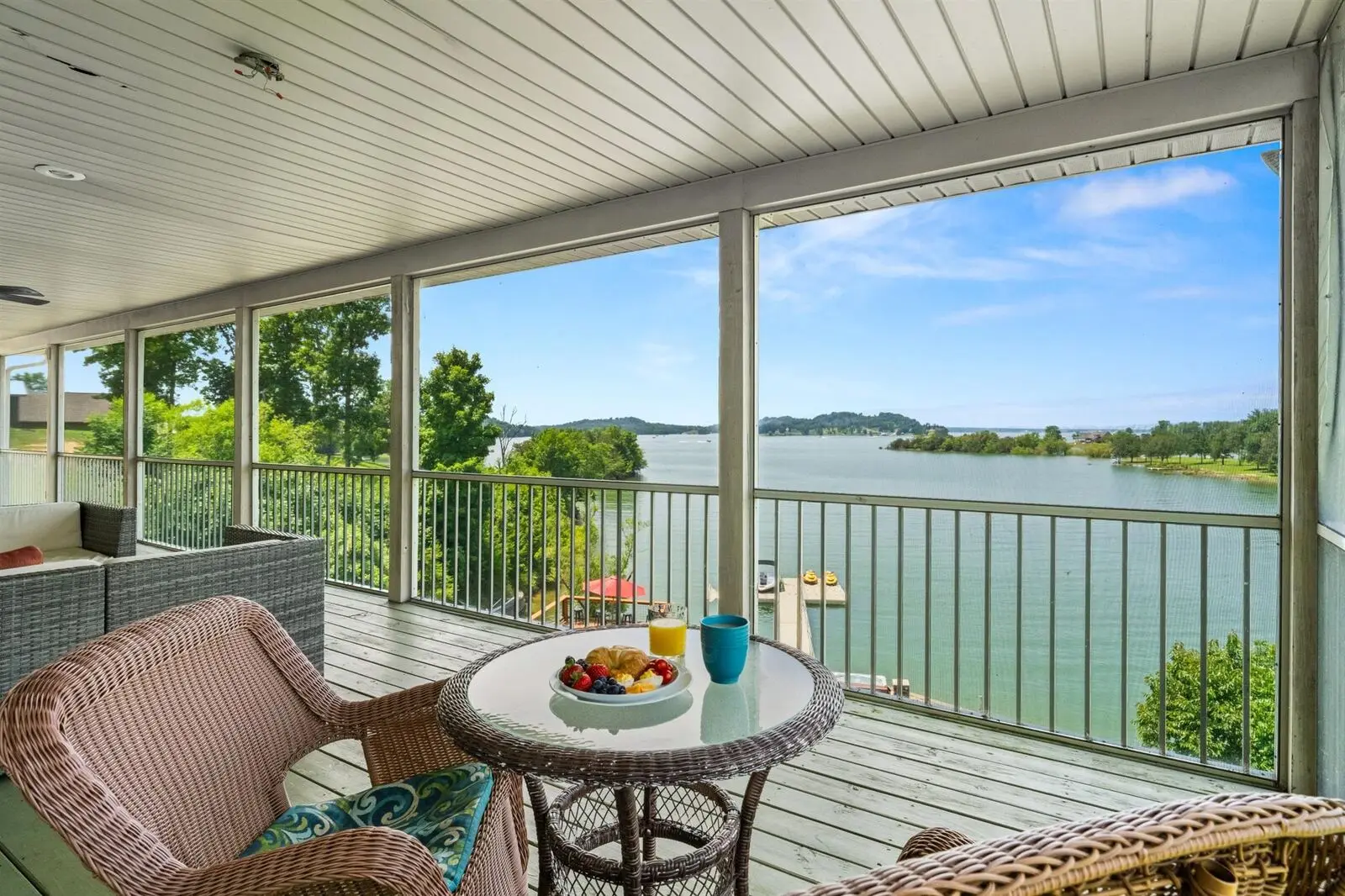 Corner of the screened porch with small wicker bistro table set with fresh fruit and orange juice, looking out through screens to a wide view of Douglas Lake on a clear day