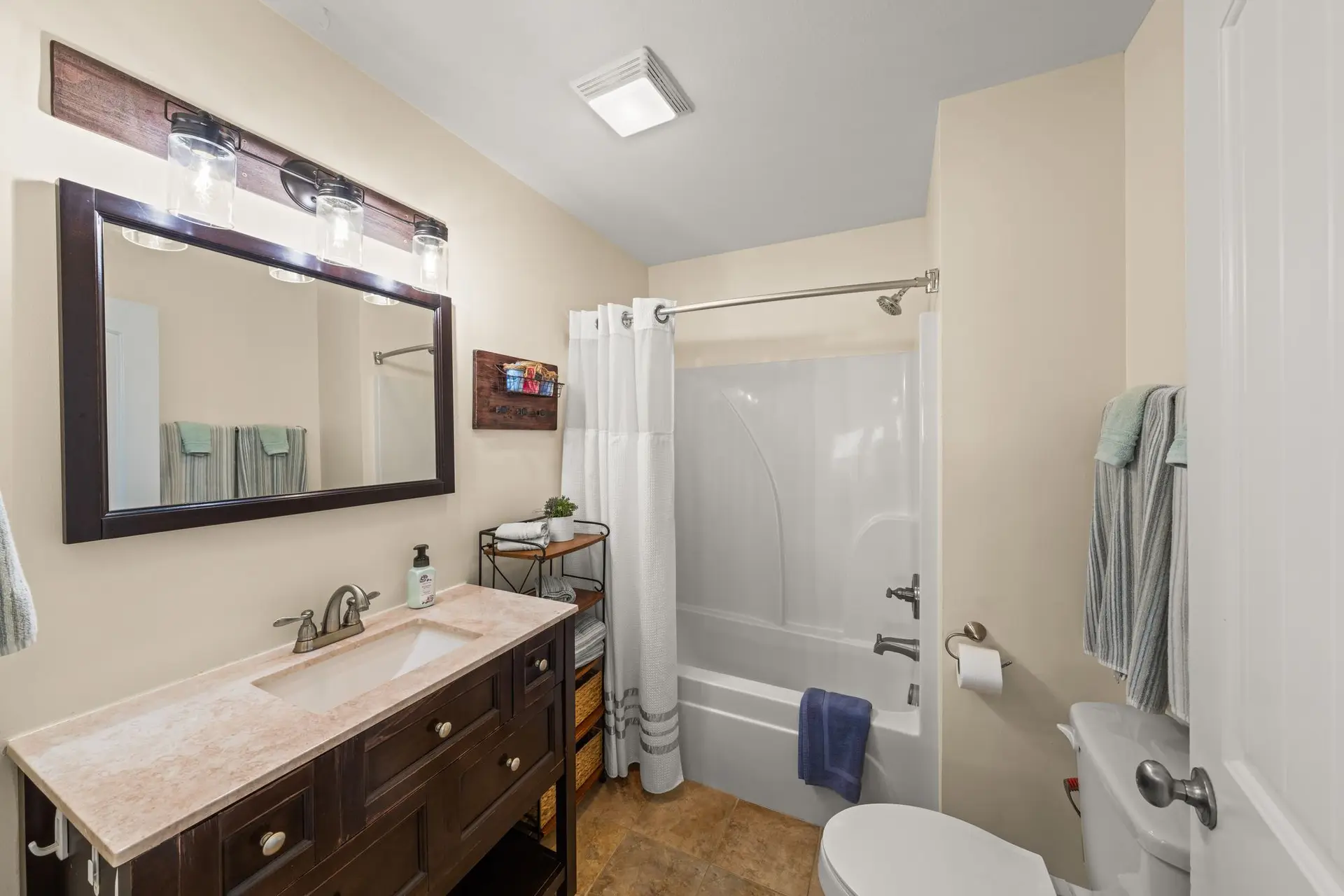 Ensuite bathroom with tub-shower combo, dark wood vanity and oversized framed mirror