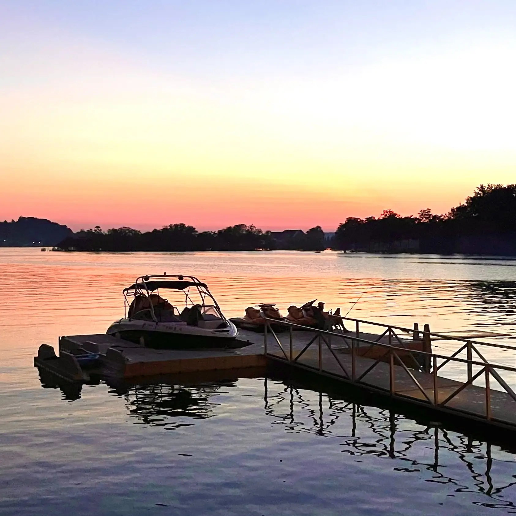 The pontoon and jet skis silhouetted at the dock against an orange sunset