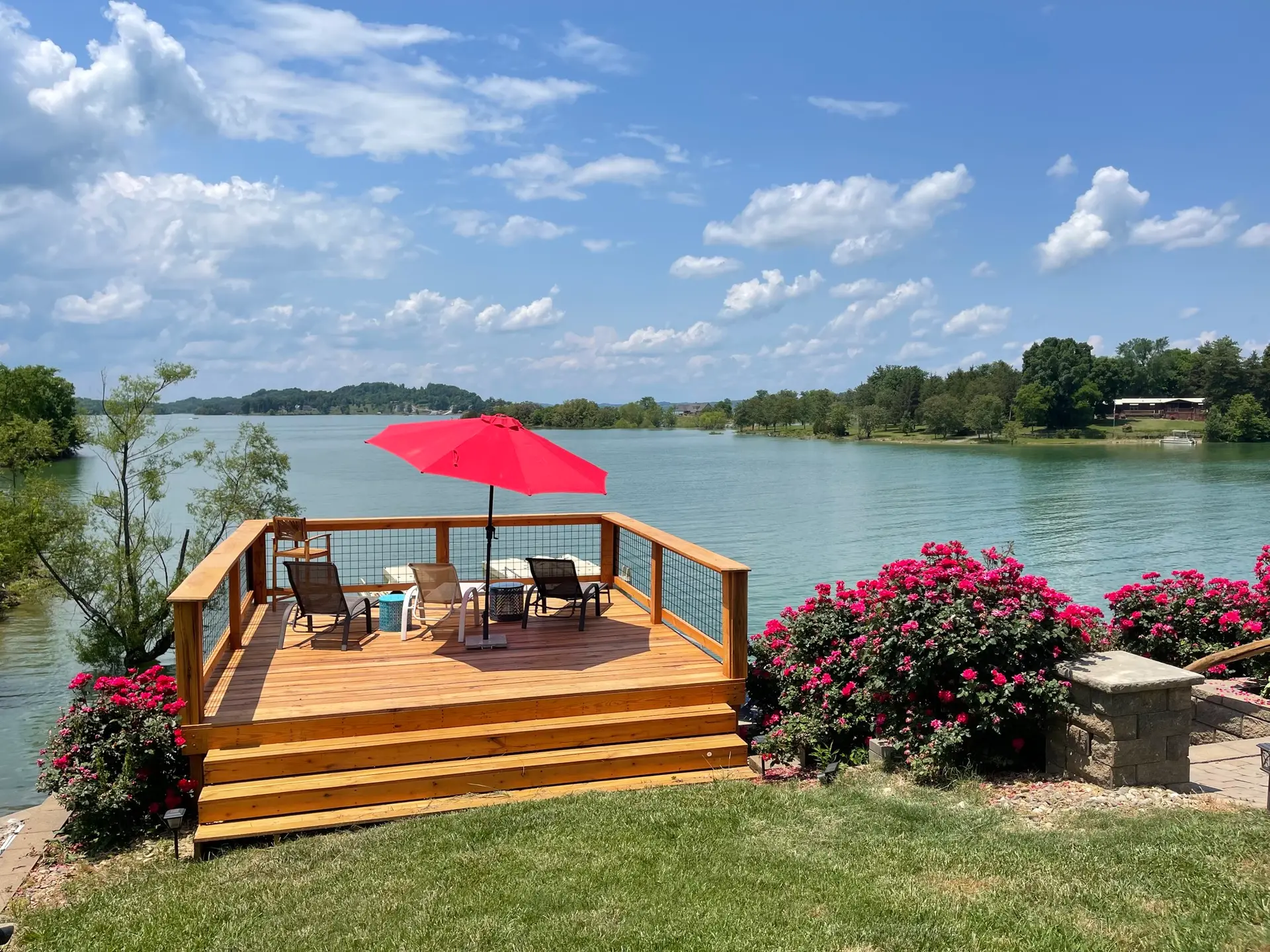 Sundeck with red umbrella surrounded by blooming rose bushes at the lake's edge