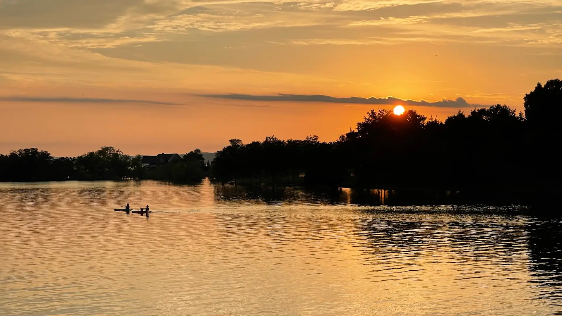 Two kayakers paddling across Douglas Lake as the sun sets behind the treeline