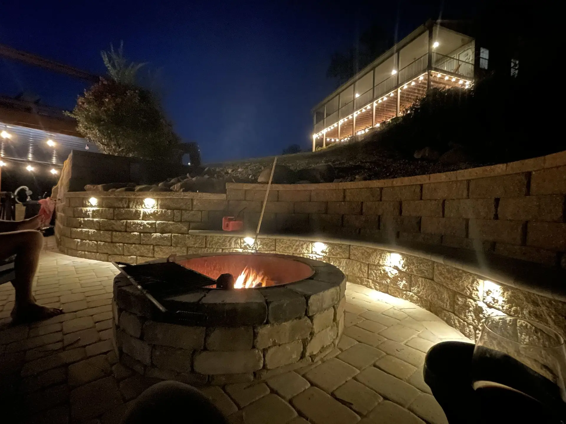 The sunken fire pit at night, retaining-wall lights glowing and the house lit up above it