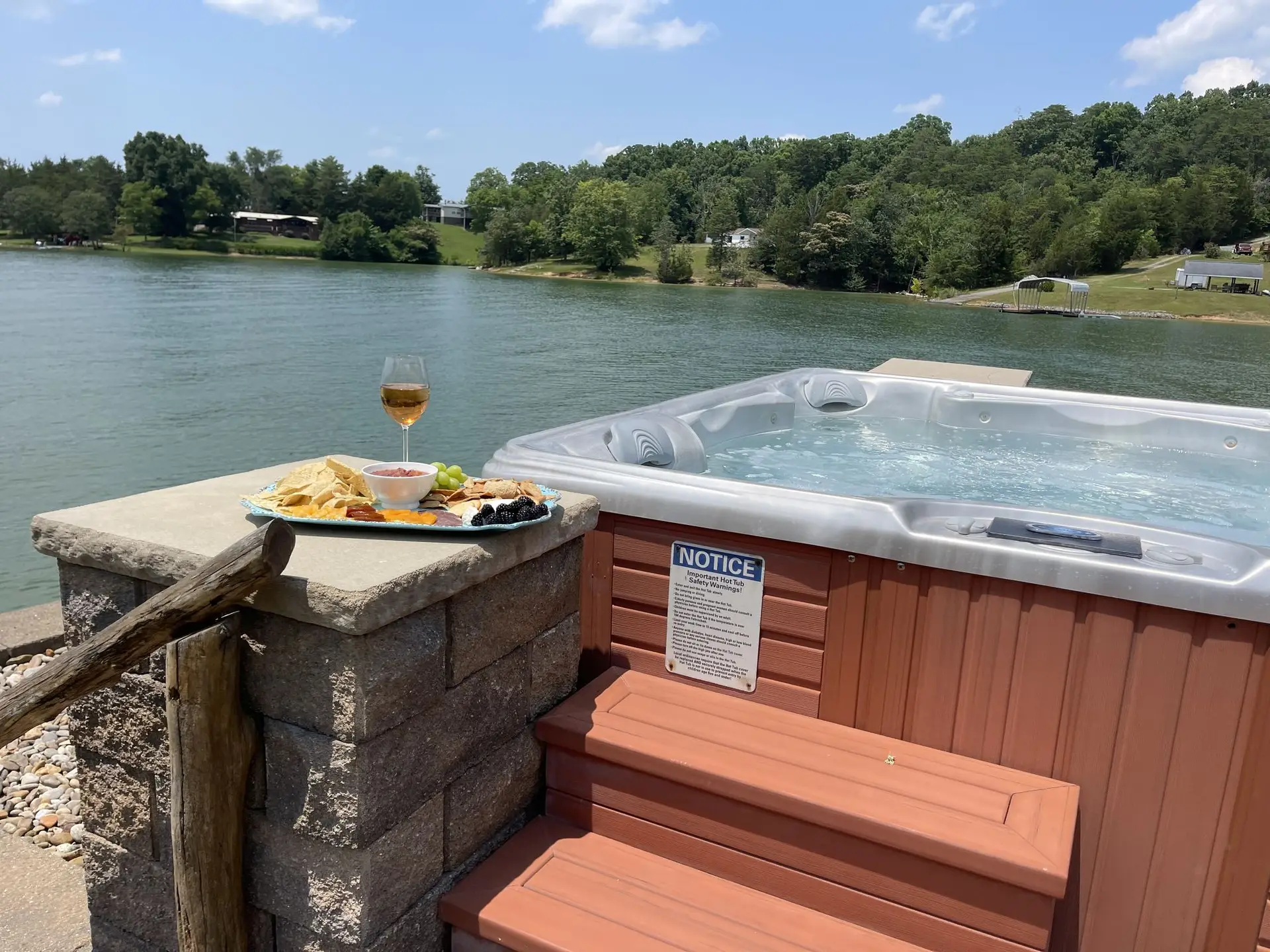 Wine and a snack plate on the stone pillar beside the lakeside hot tub on a sunny day