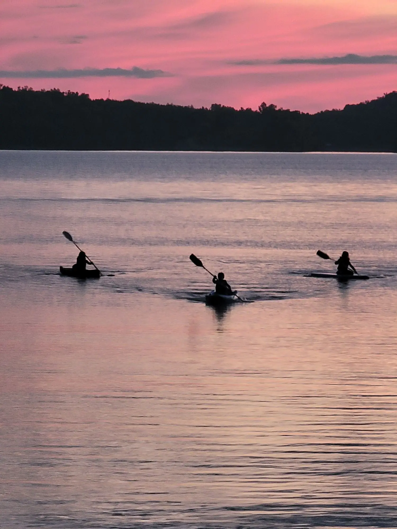 Three paddlers out on glass-calm water under a pink evening sky