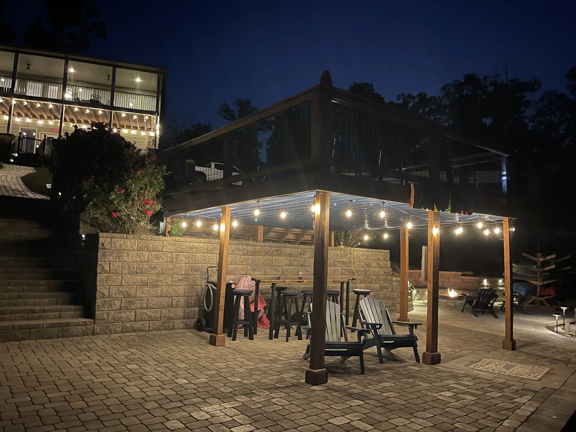The pavilion under string lights after dark with the house lit on the hill above