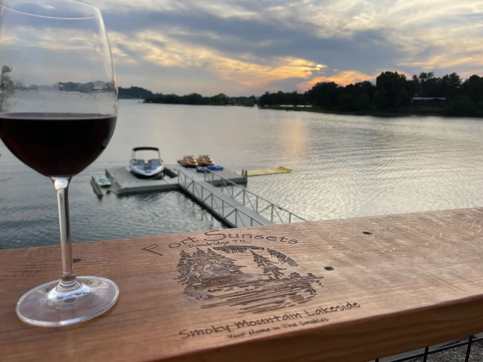 A glass of wine on the engraved Fort Sunsets table, the dock and sunset beyond