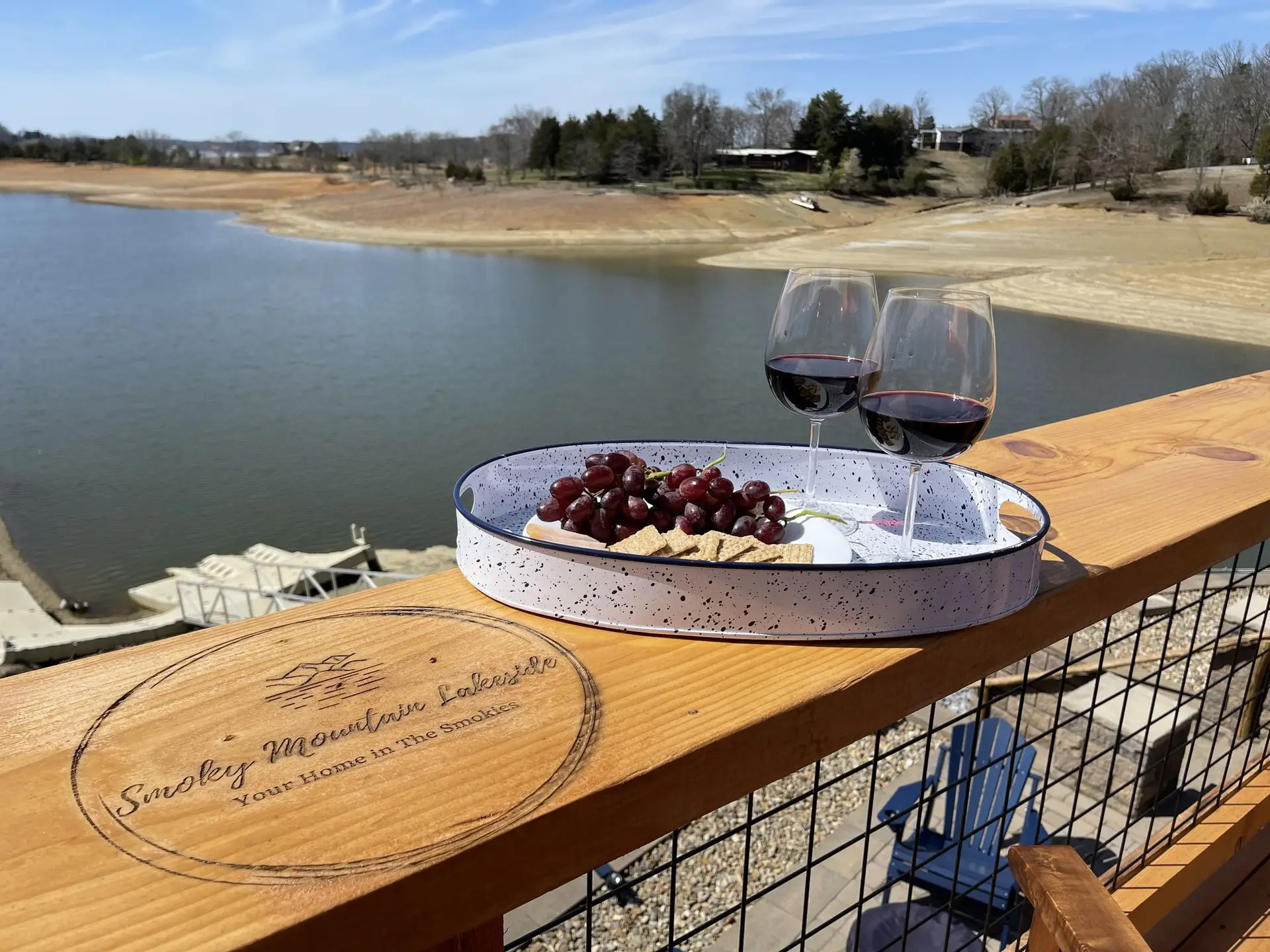 Charcuterie tray and two glasses of red wine on the sundeck railing engraved with the Smoky Mountain Lakeside logo